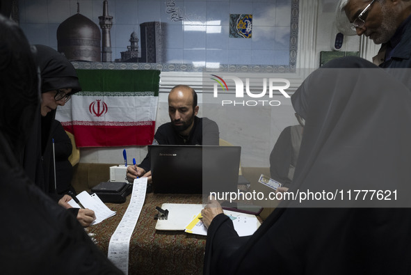 A veiled Iranian woman and Iranian men check a donated gold plaque and bank receipts for donated money during a charity ceremony to help the...