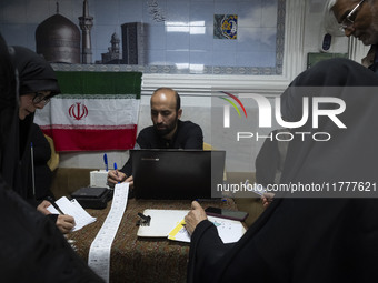 A veiled Iranian woman and Iranian men check a donated gold plaque and bank receipts for donated money during a charity ceremony to help the...