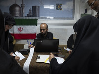 A veiled Iranian woman and Iranian men check a donated gold plaque and bank receipts for donated money during a charity ceremony to help the...