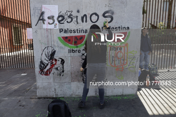 A pro-Palestine activist in Mexico City, Mexico, paints graffiti outside the Memory and Tolerance Museum, where more people demand Claudia S...