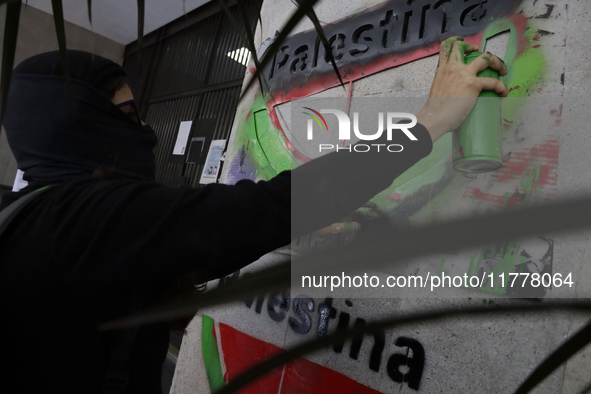 A pro-Palestine activist in Mexico City, Mexico, paints graffiti outside the Ministry of Foreign Affairs, where more people demand that Clau...