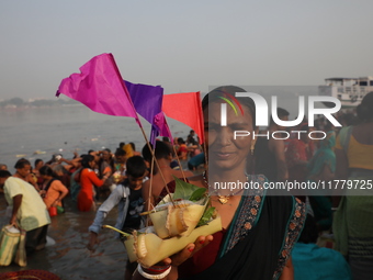 A Hindu man holds up a small decorated boat made with a banana stem as people gather to take a holy dip in the river Ganges on the occasion...