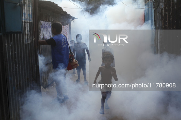 Children play in the smoke at a slum in the capital city of Dhaka, Bangladesh, as a worker sprays pesticide to kill mosquitoes. The country...