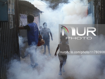 Children play in the smoke at a slum in the capital city of Dhaka, Bangladesh, as a worker sprays pesticide to kill mosquitoes. The country...