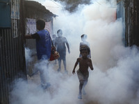 Children play in the smoke at a slum in the capital city of Dhaka, Bangladesh, as a worker sprays pesticide to kill mosquitoes. The country...