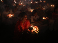 Hindu devotees sit together in front of oil lamps and pray to Shri Shri Loknath Brahmachari, a Hindu saint and philosopher, as they observe...