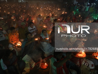 Hindu devotees sit together in front of oil lamps and pray to Shri Shri Loknath Brahmachari, a Hindu saint and philosopher, as they observe...