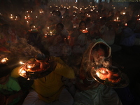 Hindu devotees sit together in front of oil lamps and pray to Shri Shri Loknath Brahmachari, a Hindu saint and philosopher, as they observe...