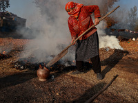 Rafiqa, 46, puts burning charcoal in a firepot on a cold day in Sopore, Jammu and Kashmir, India, on November 17, 2024. People burn fallen d...