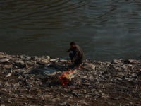 Young boys burn trash to stay warm as they brave the chilly weather to catch fish on the banks of Wular Lake in Sopore, Jammu and Kashmir, I...