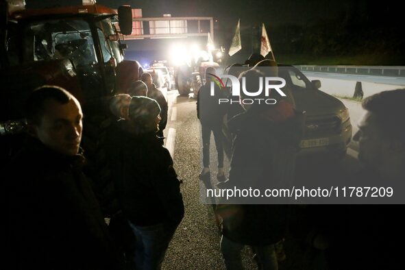 Farmers of the FNSEA (Federation Nationale des syndicats d'exploitants agricoles) union gather next to their tractors on the RN118 road at t...