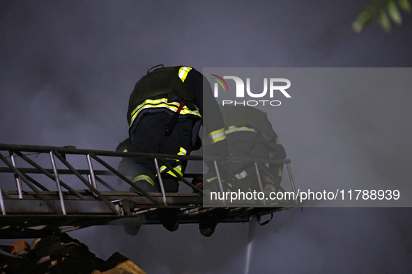 Firefighters climb a ladder to suppress a fire in a three-story residential building damaged by a Russian missile and drone attack in centra...