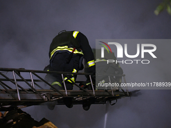 Firefighters climb a ladder to suppress a fire in a three-story residential building damaged by a Russian missile and drone attack in centra...