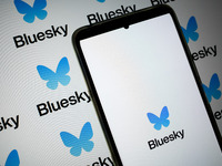 The Bluesky logo appears on a smartphone screen and as a background on a computer screen in this photo illustration in Athens, Greece, on No...