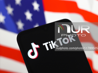 The logo of the social network TikTok appears on the screen of a smartphone, and in the background, the flag of the United States is display...