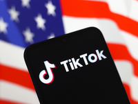 The logo of the social network TikTok appears on the screen of a smartphone, and in the background, the flag of the United States is display...