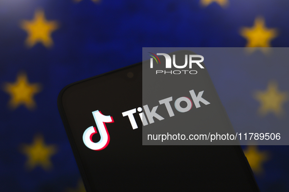 The logo of the social network TikTok appears on the screen of a smartphone, and in the background, the flag of the European Union (EU) is d...