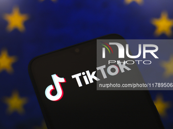 The logo of the social network TikTok appears on the screen of a smartphone, and in the background, the flag of the European Union (EU) is d...