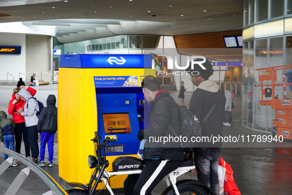 Two men interact with a bright yellow and blue ticket machine from the Dutch Railways (NS) inside Arnhem Central Station in Arnhem, Netherla...