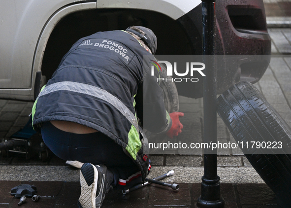 KRAKOW, POLAND - NOVEMBER 18:   
Member of roadside assistance (Polish: Pomoc Drogowa) changing a tire on a car parked in Krakow's Old Town,...