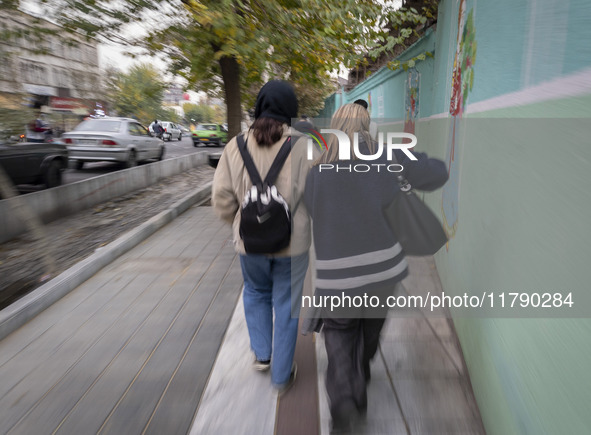 Two young Iranian women, one of whom is not wearing a mandatory headscarf, walk together along a sidewalk in downtown Tehran, Iran, on Novem...