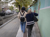 Two young Iranian women, one of whom is not wearing a mandatory headscarf, walk together along a sidewalk in downtown Tehran, Iran, on Novem...