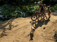 Tribal children ride on a bicycle as a puppy runs beside them in Durgapur, Netrokona, Bangladesh, on November 17, 2024. (