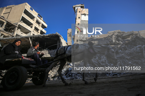 Palestinians ride a donkey-drawn cart next to the rubble of a house destroyed in previous airstrikes during the Israeli military offensive,...