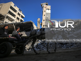 Palestinians ride a donkey-drawn cart next to the rubble of a house destroyed in previous airstrikes during the Israeli military offensive,...