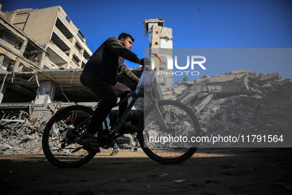 A Palestinian young man rides a bicycle next to the rubble of a house destroyed in previous airstrikes during the Israeli military offensive...