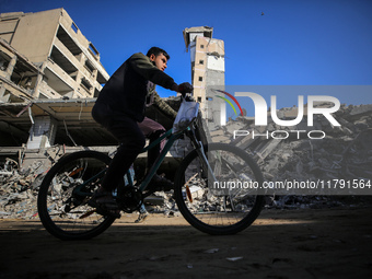 A Palestinian young man rides a bicycle next to the rubble of a house destroyed in previous airstrikes during the Israeli military offensive...