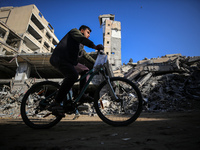 A Palestinian young man rides a bicycle next to the rubble of a house destroyed in previous airstrikes during the Israeli military offensive...