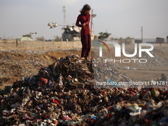 A displaced Palestinian girl searches through a pile of garbage in Khan Yunis, Gaza Strip, on November 19, 2024, amid the ongoing war betwee...