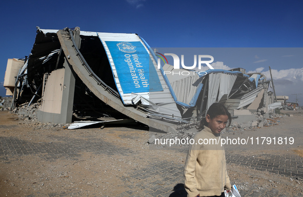 A displaced Palestinian girl walks past a damaged World Health Organisation storage center hit in recent Israeli bombardment in Khan Yunis,...