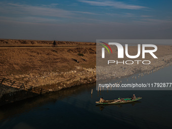 A boy rides a bicycle as fishermen row a boat in Wular Lake in Sopore, Jammu and Kashmir, India, on November 19, 2024. (