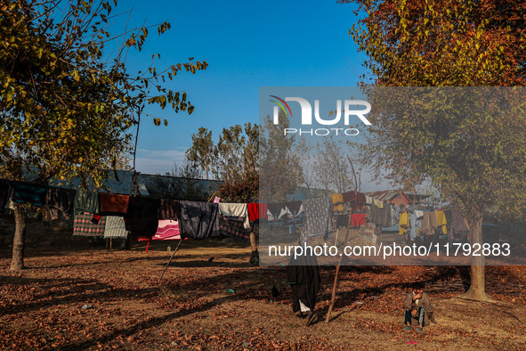 A man sits as clothes are kept for sun drying on an autumn day in Sopore, Jammu and Kashmir, India, on November 19, 2024. 