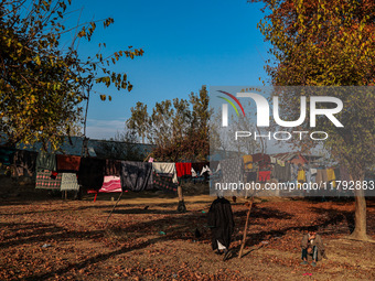 A man sits as clothes are kept for sun drying on an autumn day in Sopore, Jammu and Kashmir, India, on November 19, 2024. (