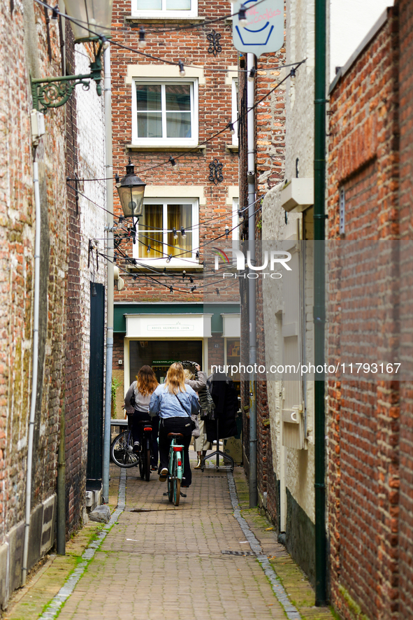 In Venlo, Netherlands, on July 28, 2023, two cyclists pass through a narrow alleyway adorned with historic brick facades and twinkling strin...