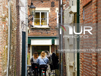 In Venlo, Netherlands, on July 28, 2023, two cyclists pass through a narrow alleyway adorned with historic brick facades and twinkling strin...