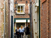 In Venlo, Netherlands, on July 28, 2023, two cyclists pass through a narrow alleyway adorned with historic brick facades and twinkling strin...