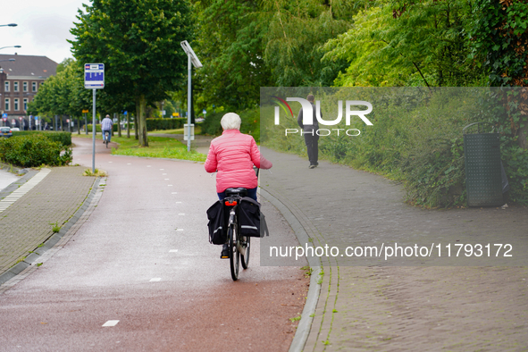 A senior woman in a bright pink jacket cycles on a well-maintained bike path in Venlo, Netherlands, on July 28, 2023. The scene highlights t...