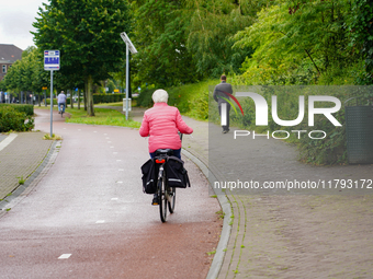 A senior woman in a bright pink jacket cycles on a well-maintained bike path in Venlo, Netherlands, on July 28, 2023. The scene highlights t...