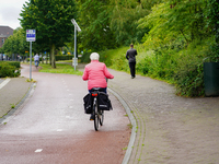 A senior woman in a bright pink jacket cycles on a well-maintained bike path in Venlo, Netherlands, on July 28, 2023. The scene highlights t...