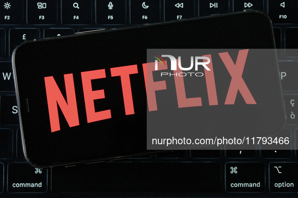 The Netflix logo displays on an iPhone screen, which is placed over a MacBook Air keyboard, in an editorial image in City, Country, on Novem...