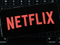 The Netflix logo displays on an iPhone screen, which is placed over a MacBook Air keyboard, in an editorial image in City, Country, on Novem...