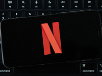 The Netflix logo displays on an iPhone screen, which is placed over a MacBook Air keyboard, in an editorial image in City, Country, on Novem...