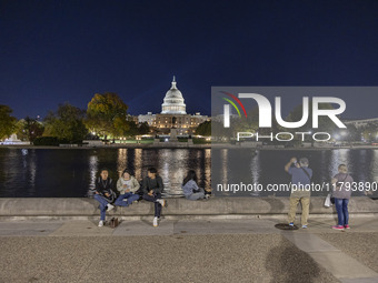 People taking photos and relaxing in front of the water. Night view of the illuminated US Capitol, the seat of the United States Congress wi...