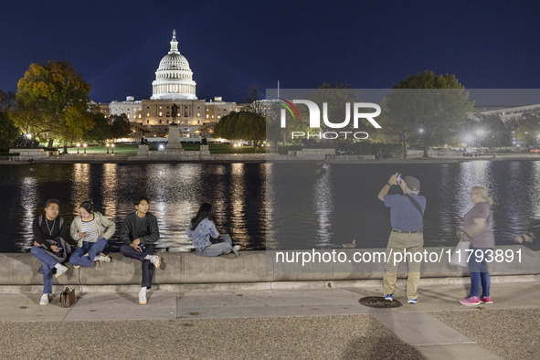 People taking photos and relaxing in front of the water. Night view of the illuminated US Capitol, the seat of the United States Congress wi...