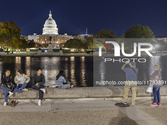 People taking photos and relaxing in front of the water. Night view of the illuminated US Capitol, the seat of the United States Congress wi...