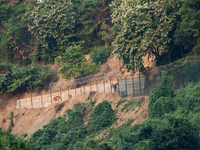 A cowboy heads home with his cow as the wall marking the border between India and Bangladesh is visible in Durgapur, Netrokona, Bangladesh,...